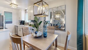 Cocina moderna con comedor, que incluye una mesa de madera, sillas, un florero con flores y una lámpara colgante.