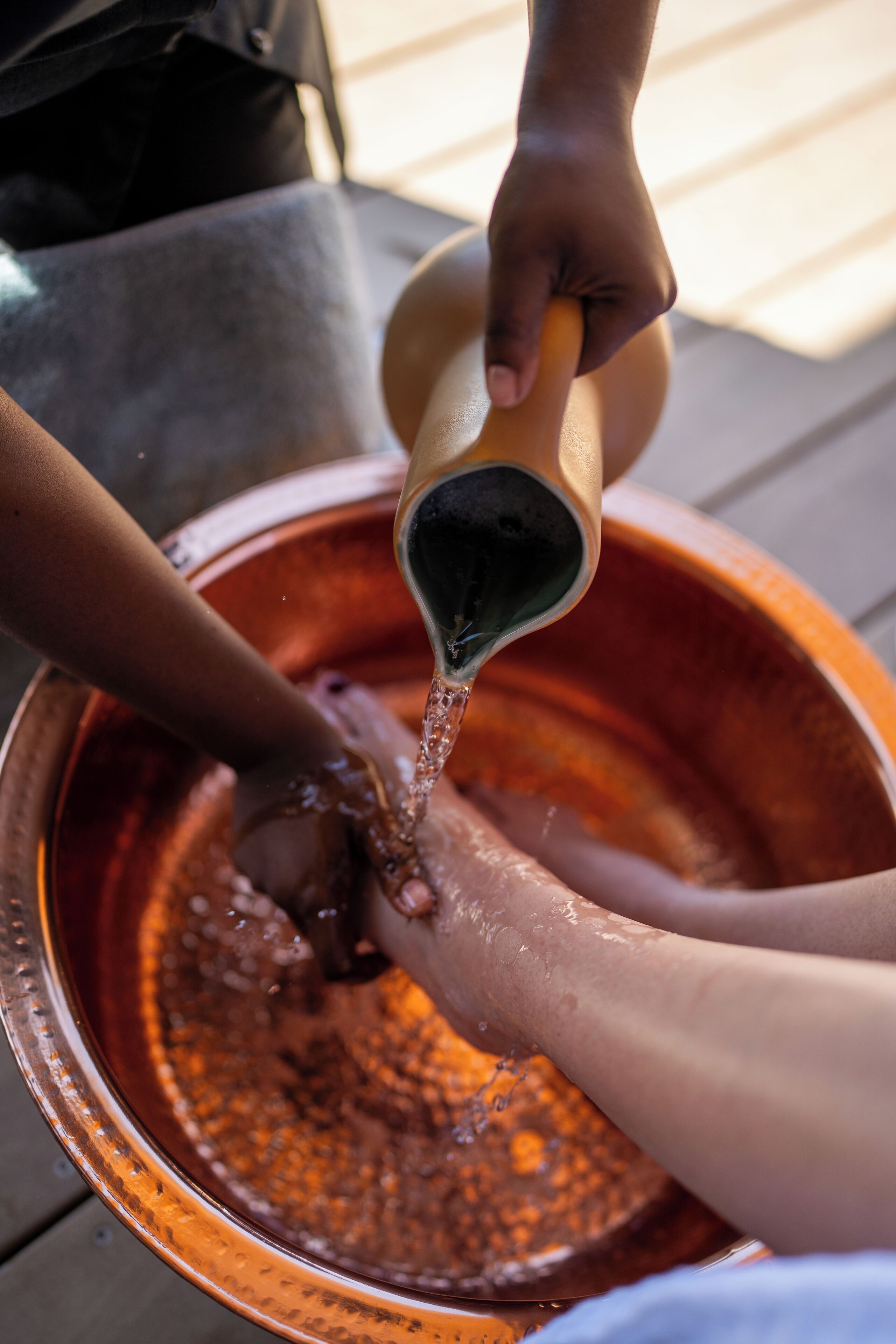 A person pouring water from a jug into a copper basin.