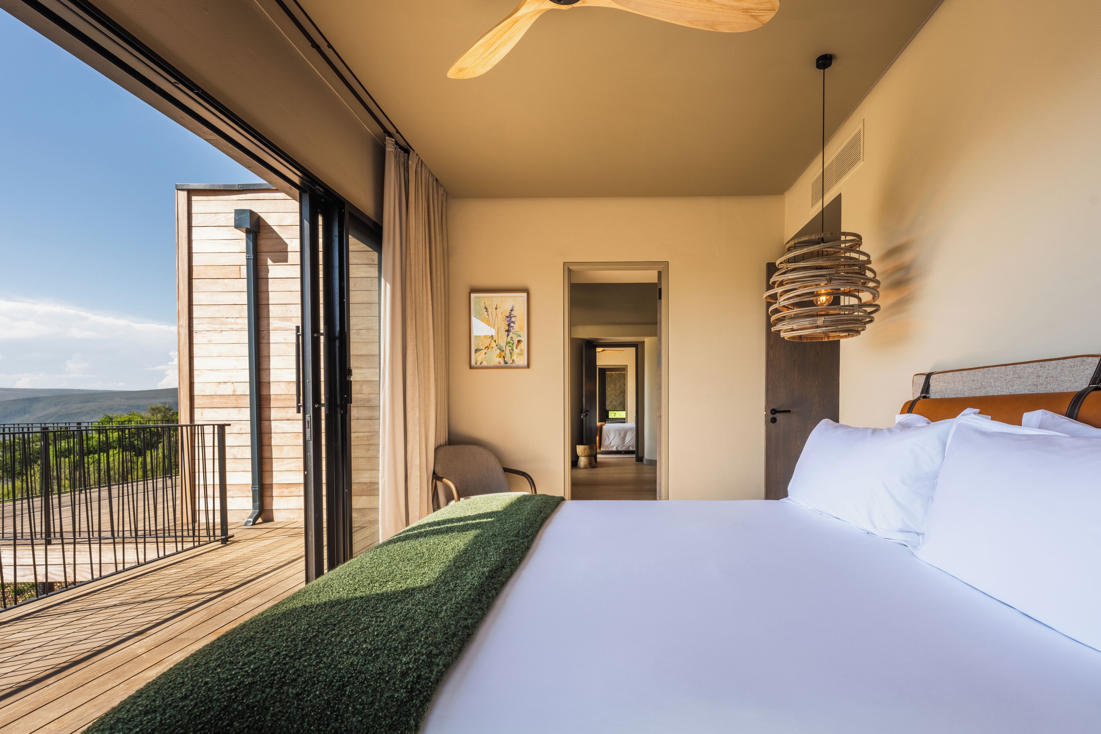Une chambre avec un grand lit, une vue sur l’extérieur, un ventilateur de plafond et un luminaire suspendu.