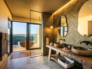 A modern bathroom with a large mirror, two sinks with stone bowls, a wooden vanity, and a view of the countryside through a glass door. - Mantis Hiddn In Addo (Gqebergha)