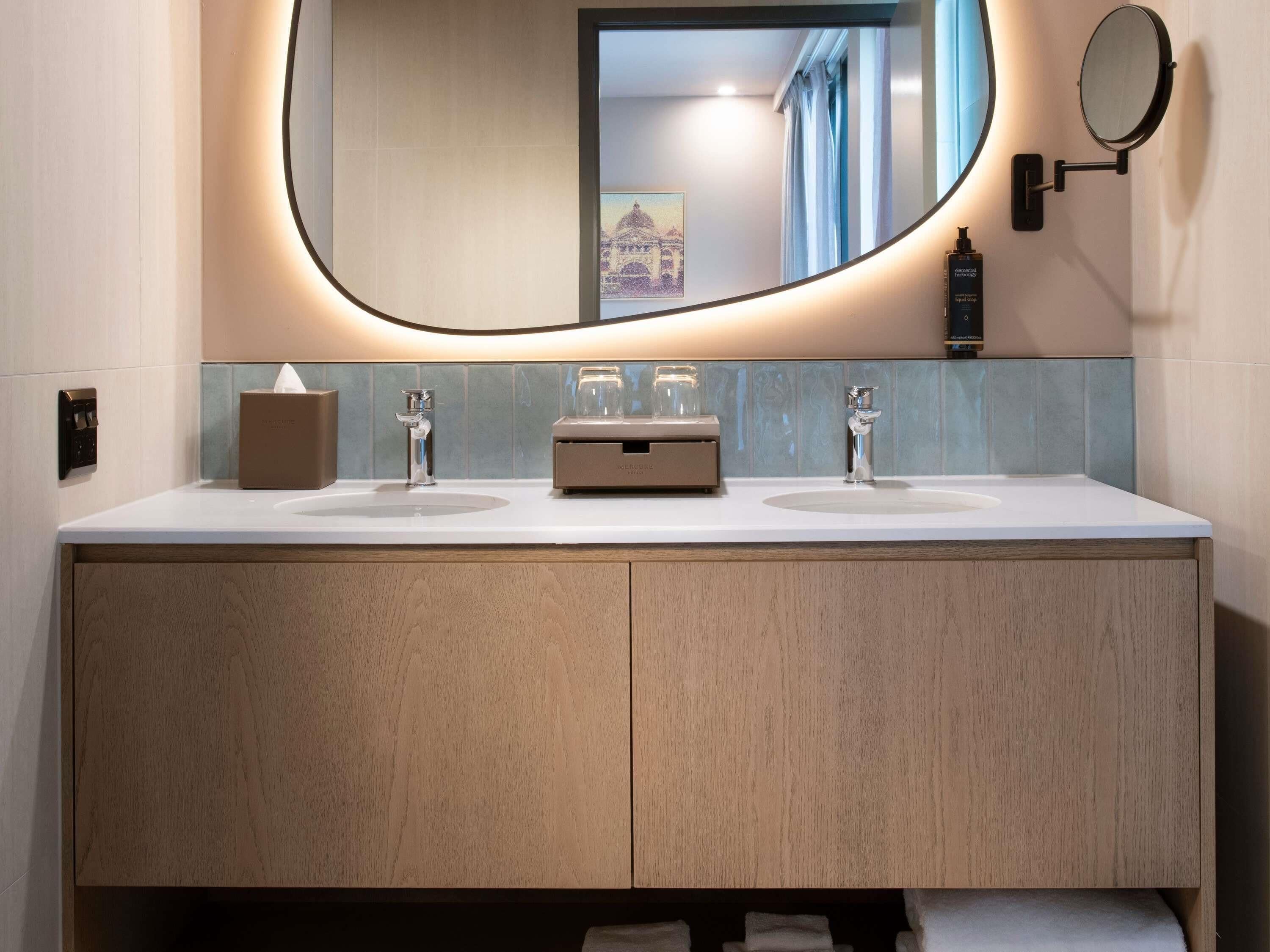 A modern bathroom with a double sink vanity, a large mirror, and a small round mirror on the wall.
