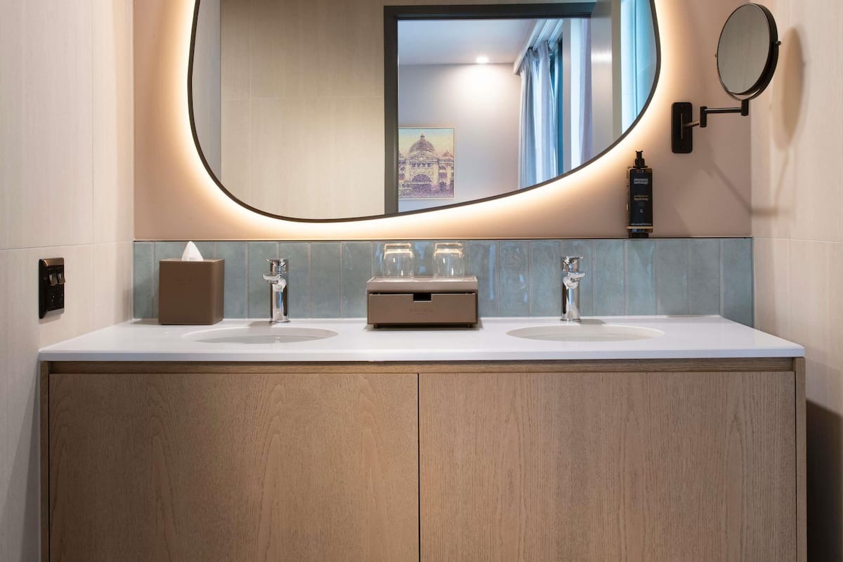 A modern bathroom with a double sink vanity, a large mirror, and a small round mirror on the wall.