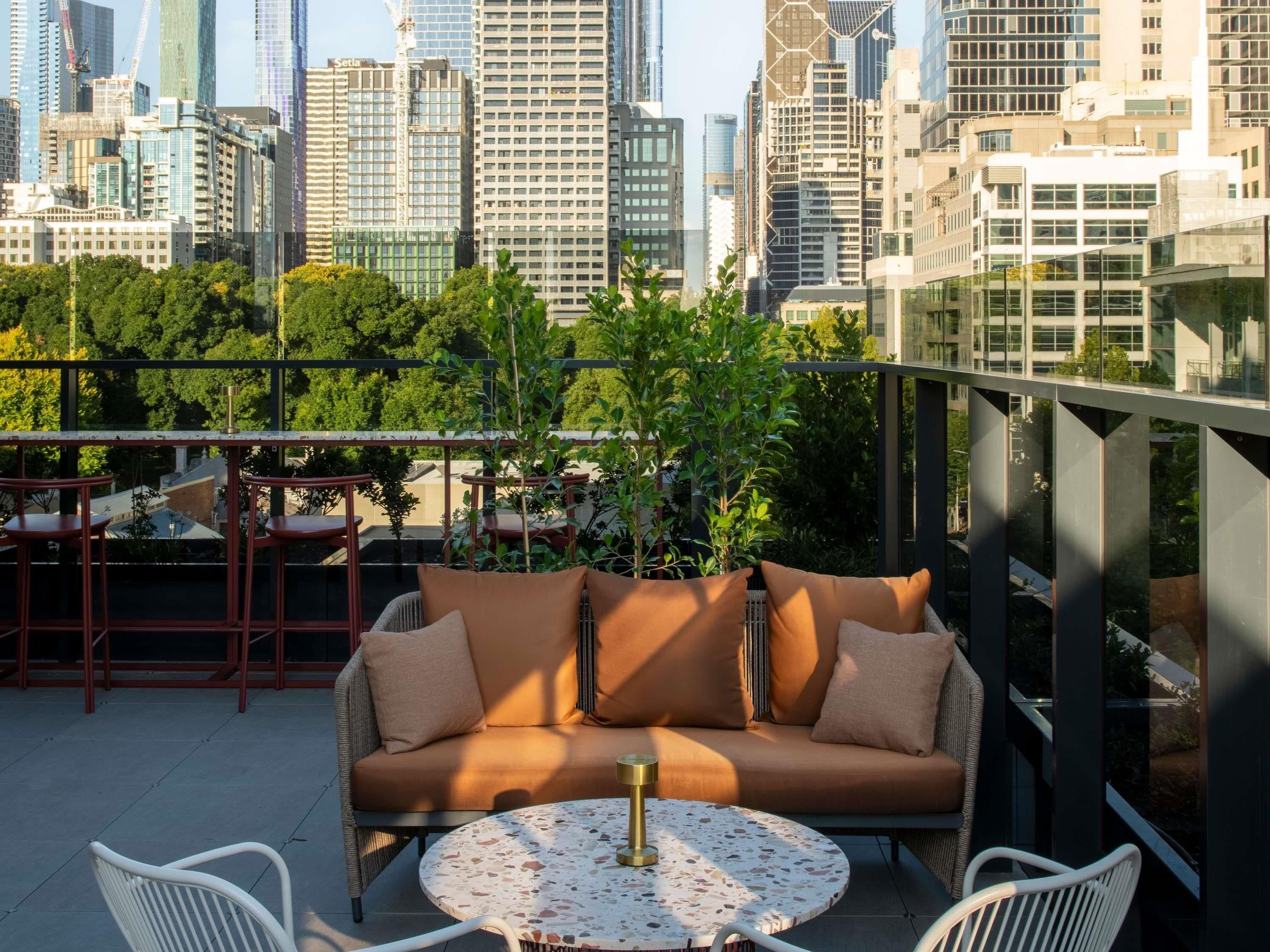 Eine Dachterrasse mit einer Couch, Stühlen und einem Tisch, mit Blick auf eine Stadtlandschaft mit modernen Gebäuden.