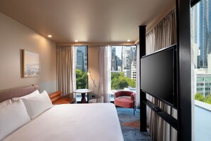 Ein Hotelzimmer mit einem großen Bett, einem kleinen Tisch, einem Sessel und einem Fernseher.