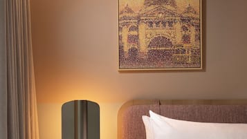 Ein Hotelzimmer mit einem Bett, einem Nachttisch mit Lampe, einem Bild eines Gebäudes und einem Vorhang.