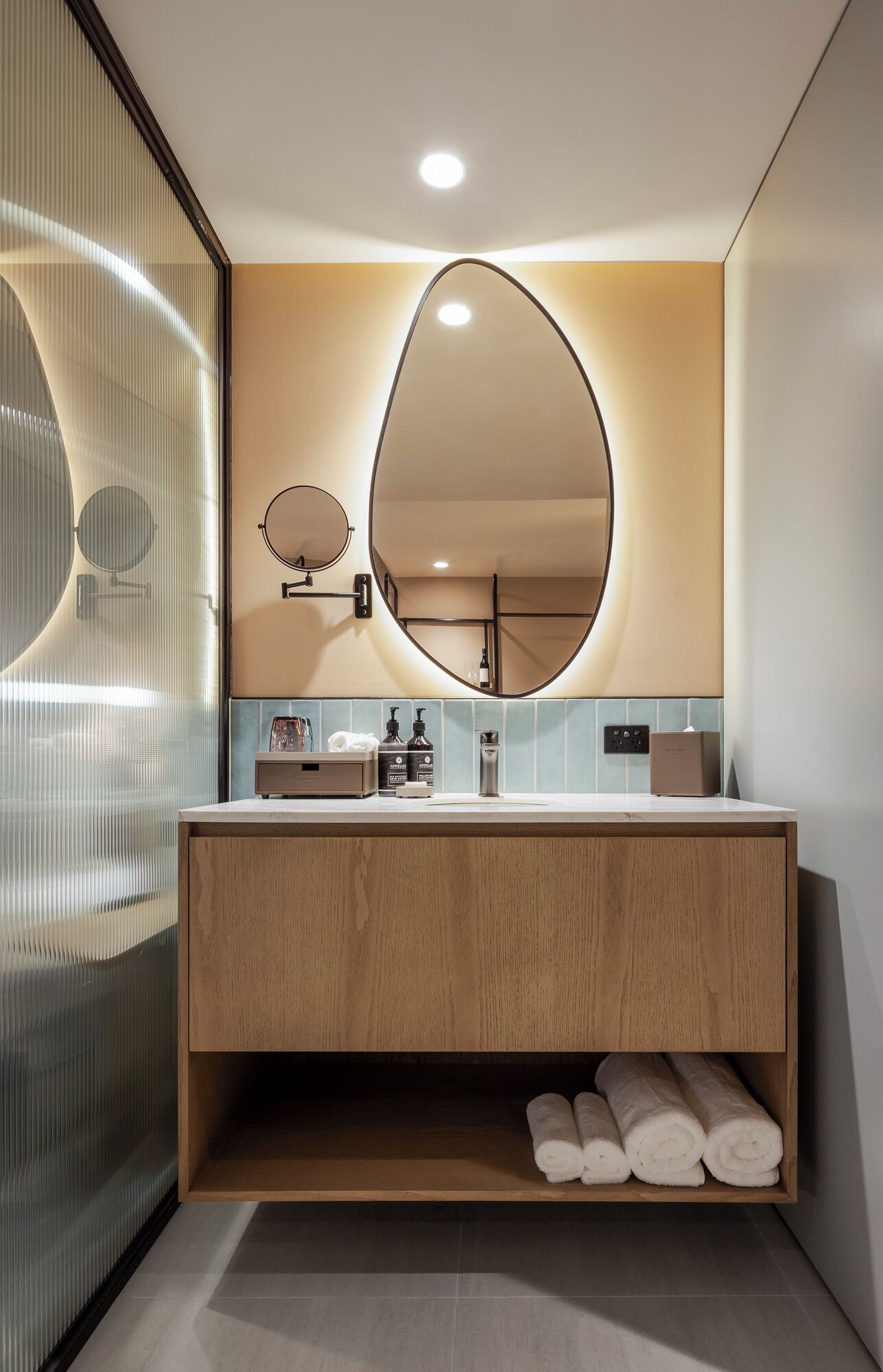 Un baño moderno con tocador de madera, un espejo ovalado grande y un perchero para toallas.