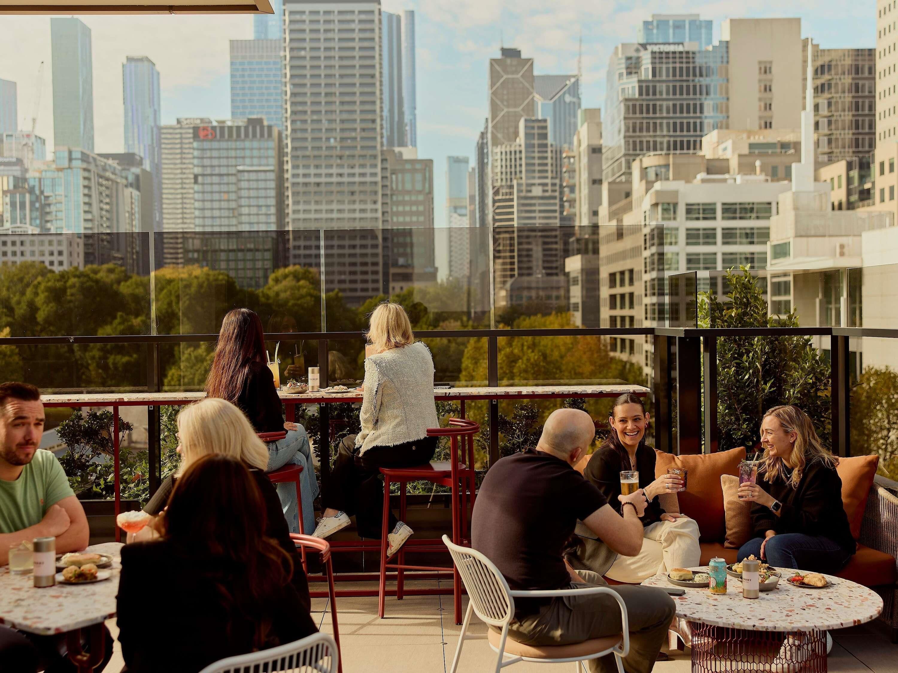 A rooftop terrace with tables and chairs, city skyline views, and a mix of modern and traditional architecture.