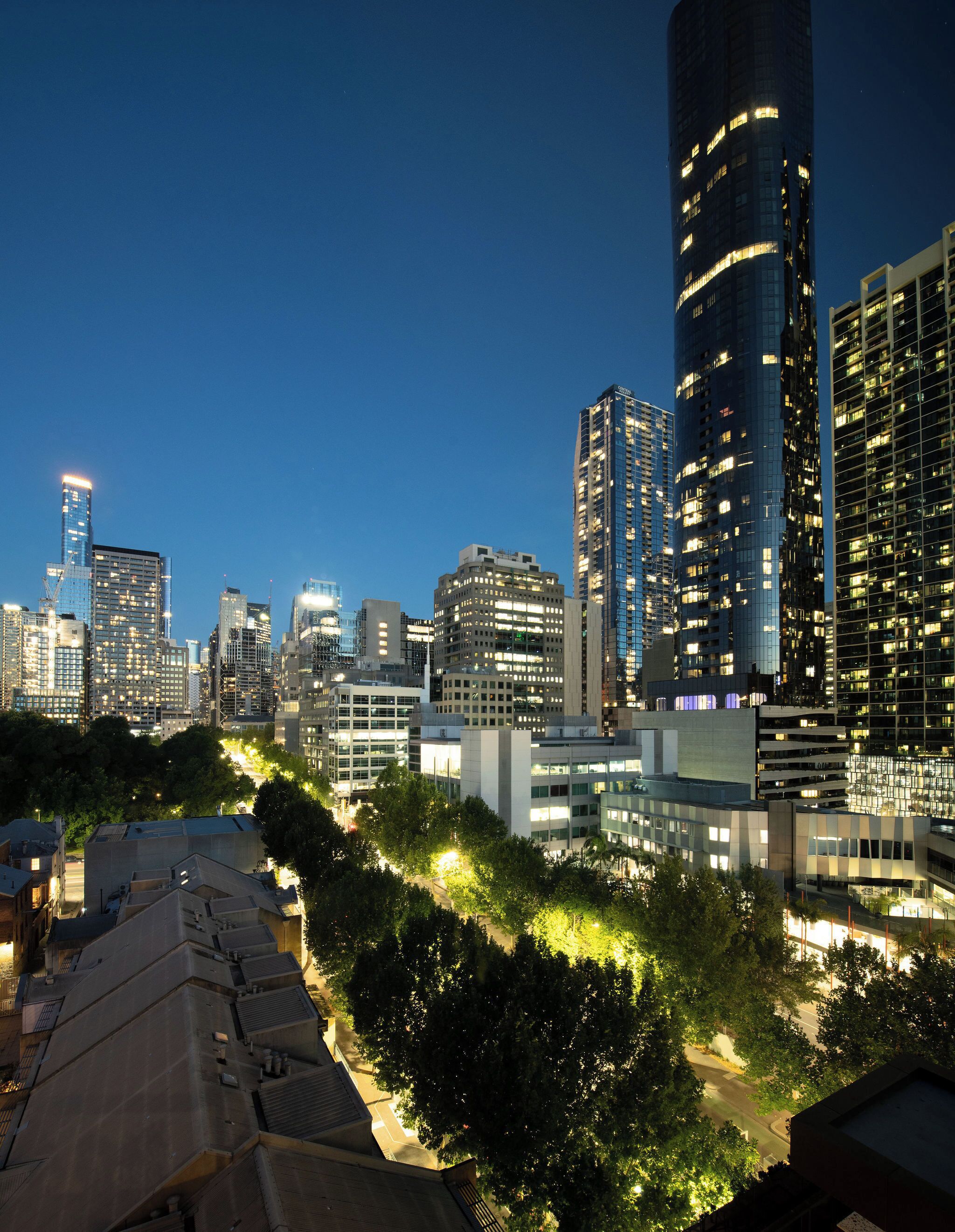 A cityscape at dusk with modern high-rise buildings, a tree-lined street, and a clear sky.