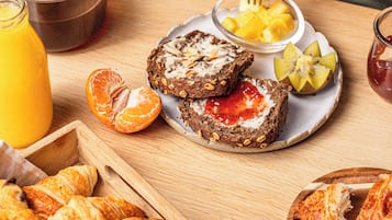 Una mesa de desayuno con cruasanes, tostadas con mermelada y miel, un vaso de jugo de naranja y un bol de fruta.