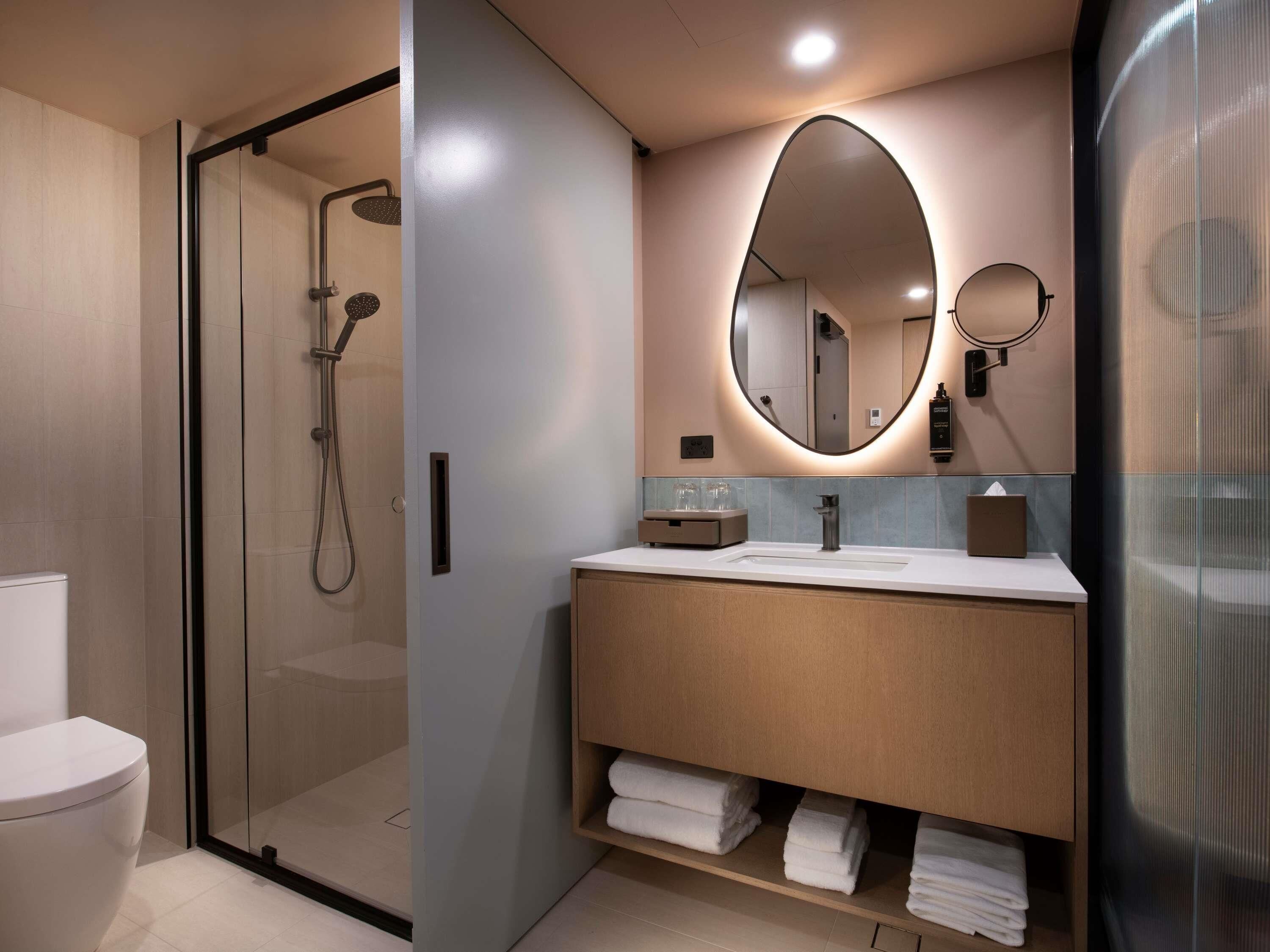 Un baño moderno con ducha acristalada, tocador con espejo y toallas dobladas con cuidado.