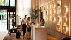 A hotel reception area with a modern design, including a reception desk, a large potted plant, and a wall with abstract art pieces. - Mercure Melbourne La Trobe Street (West Melbourne)