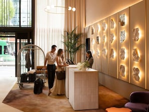 A hotel reception area with a modern design, including a reception desk, a large potted plant, and a wall with abstract art pieces. - Mercure Melbourne La Trobe Street (West Melbourne)