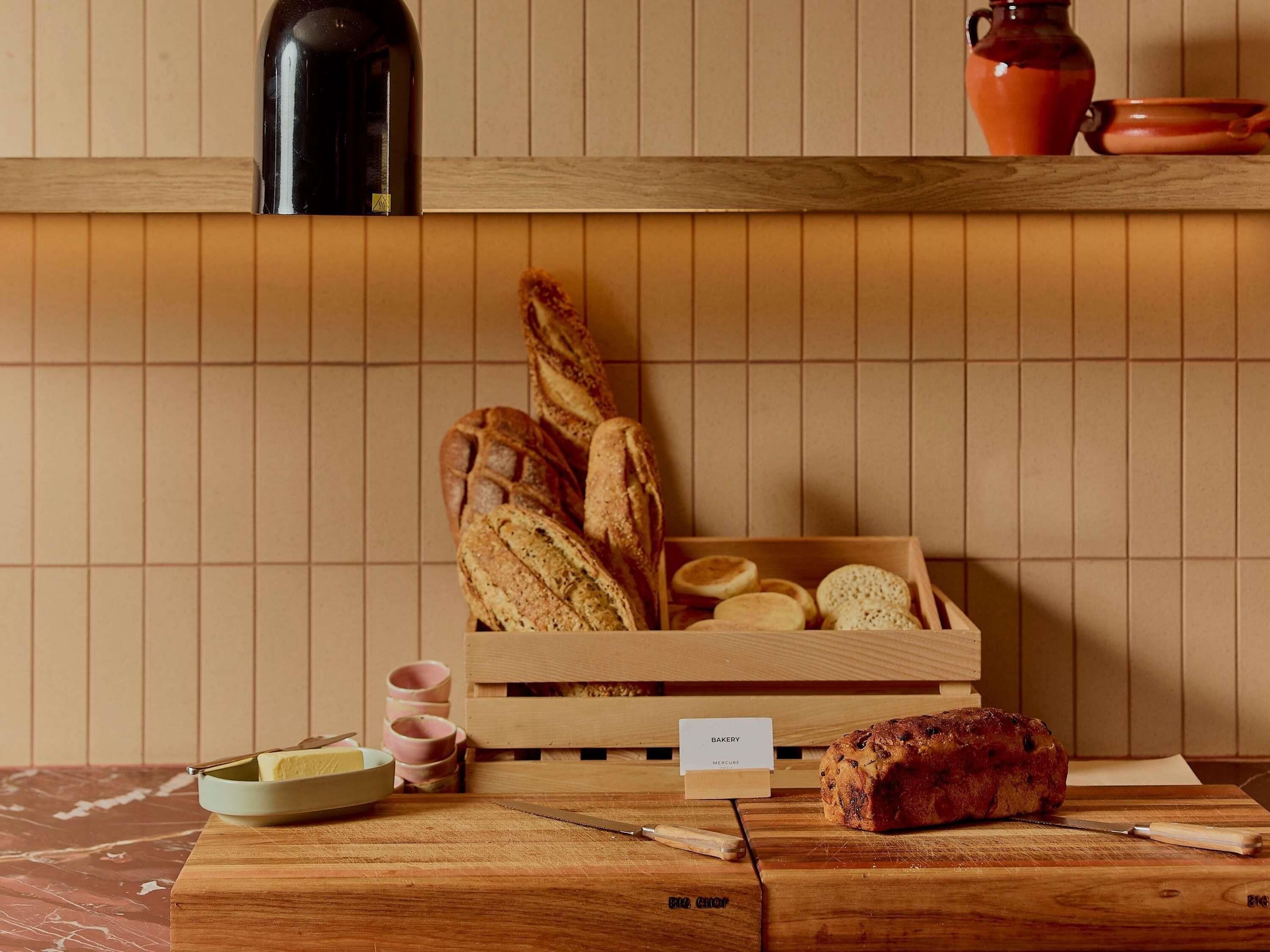 A wooden cutting board with a loaf of bread, a box of bread rolls, and a sign labeled 'BAKERY.'