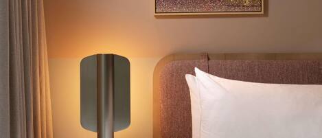 A hotel room with a bed, a nightstand with a lamp, a painting on the wall, and a window with curtains.