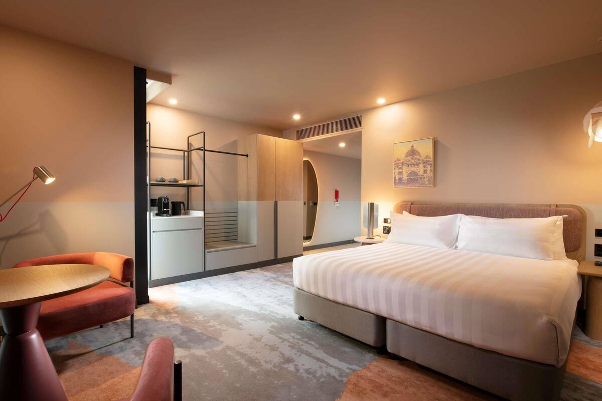 A modern hotel room with a bed, a desk, a chair, and a small table.