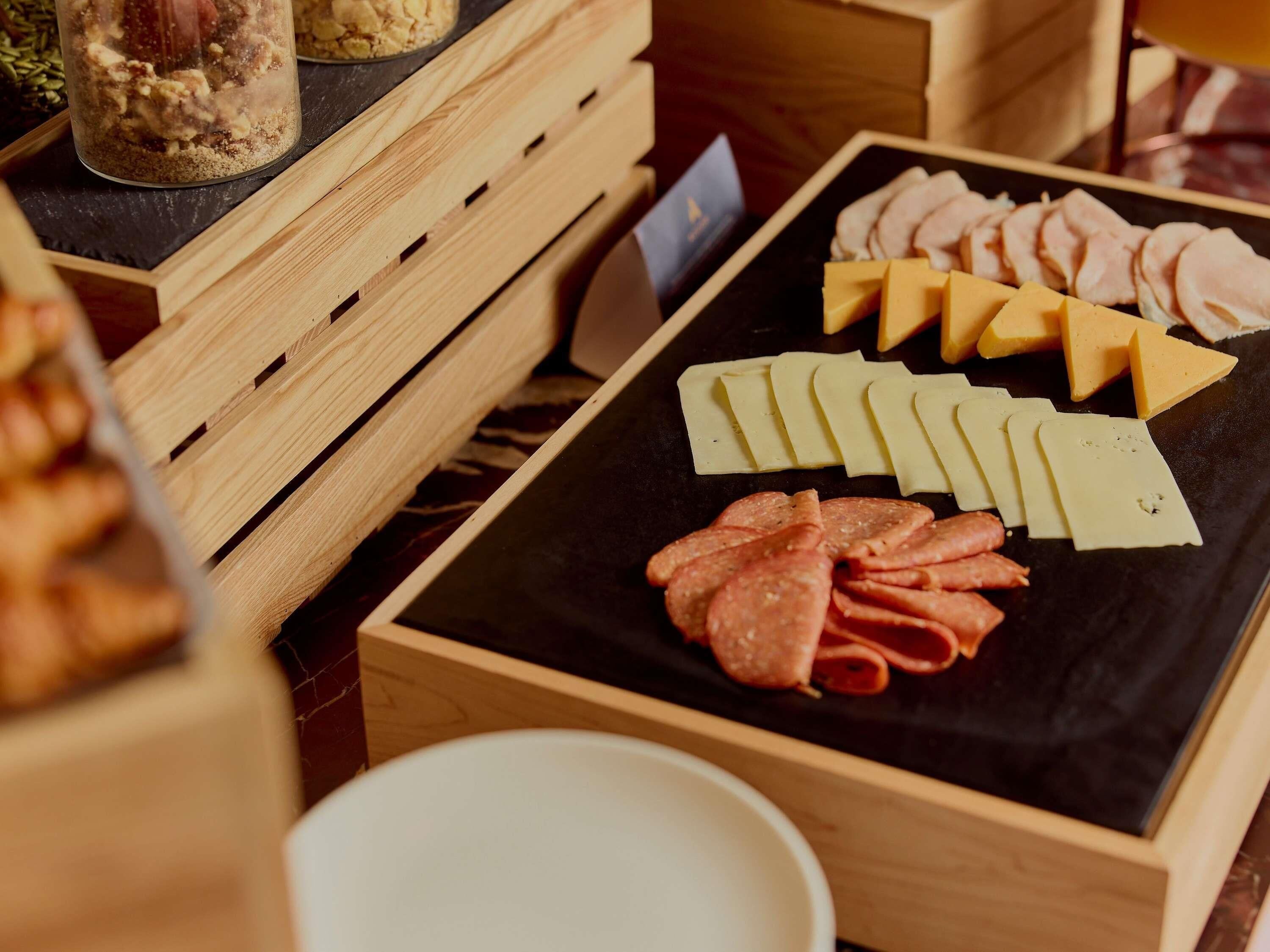 A wooden crate with a black surface containing sliced meats and cheeses.