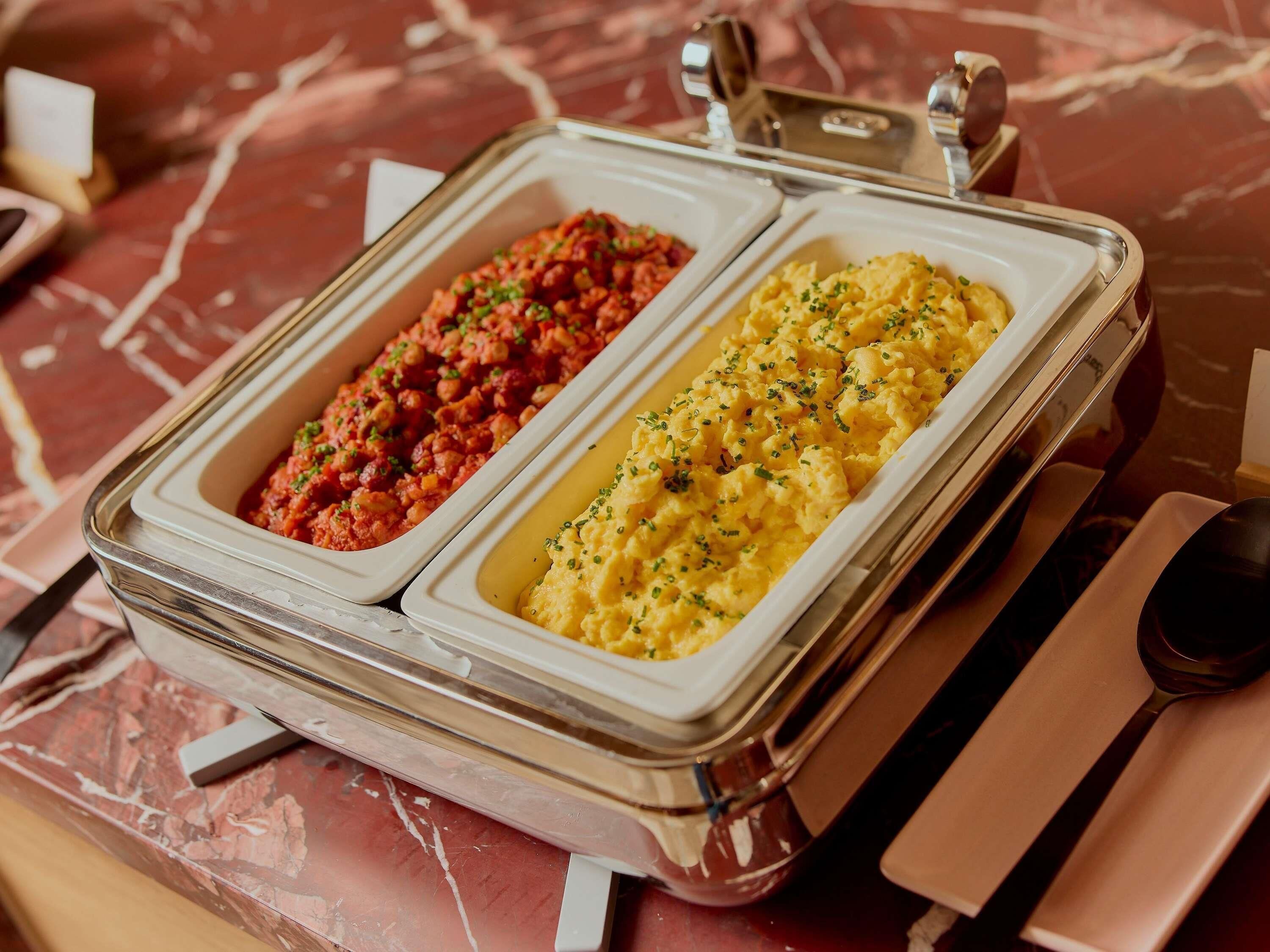 Un buffet con due piatti di portata: uno con salsa rossa e l'altro con purè di patate gialle.