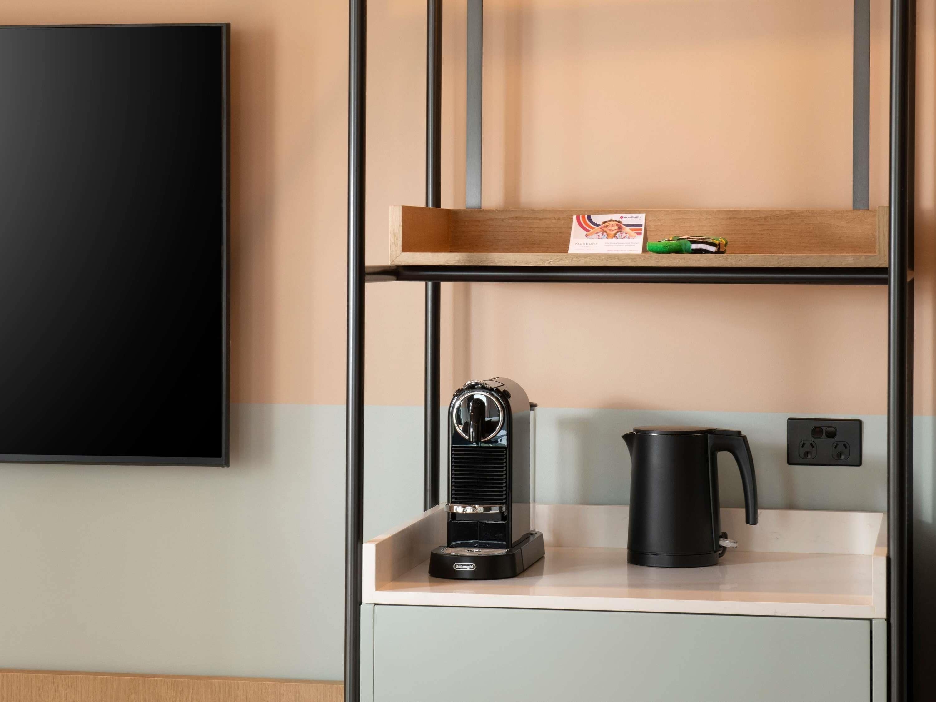 A kitchenette with a coffee maker, a kettle, and a shelf with a small item.