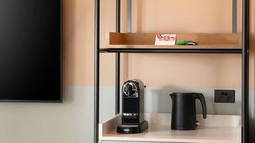 A kitchenette with a coffee maker, a kettle, and a shelf with a small item.