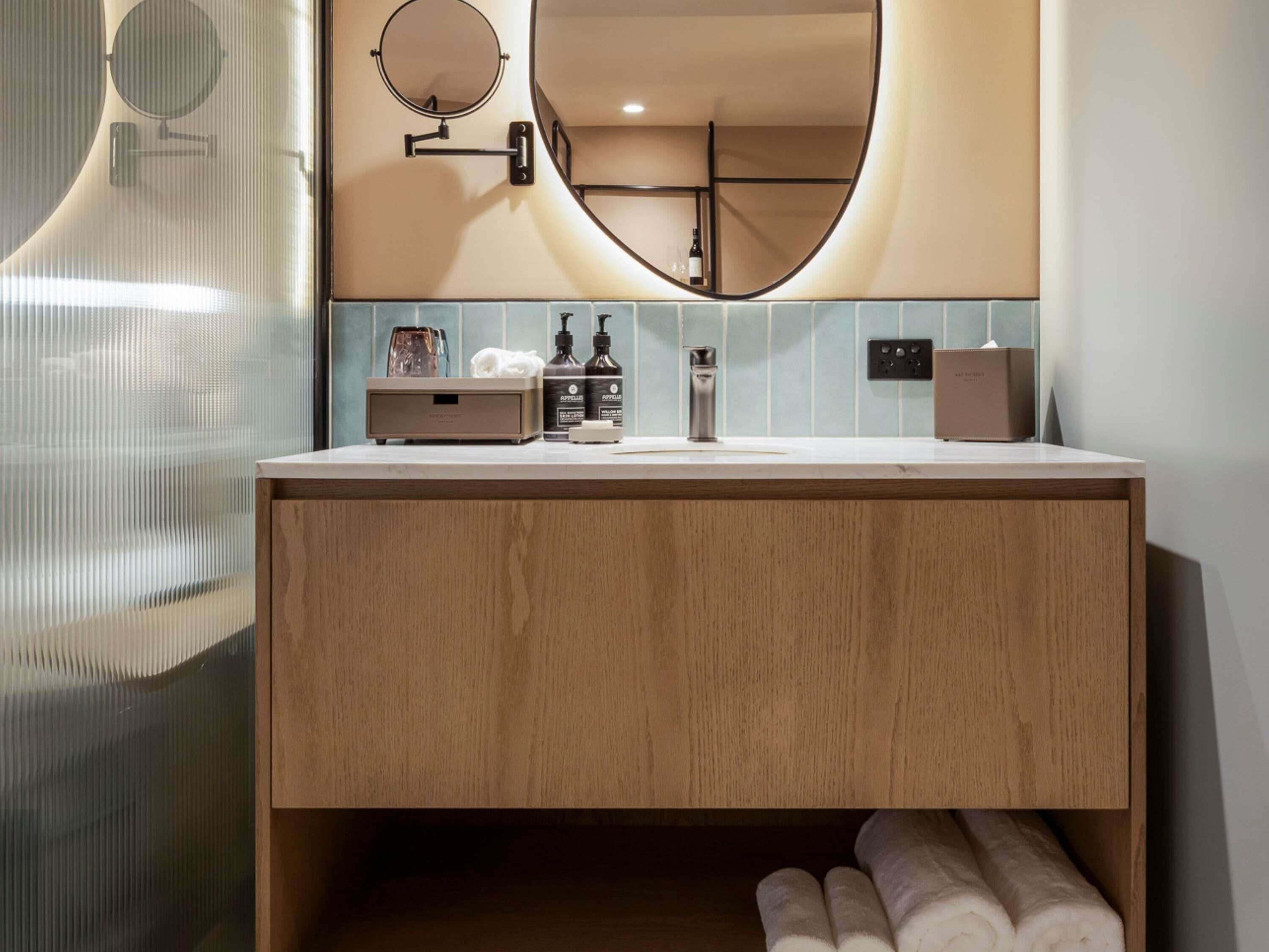 Un baño moderno con tocador de madera, un espejo redondo y un perchero para toallas.