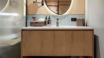 Un baño moderno con tocador de madera, un espejo redondo y un perchero para toallas.