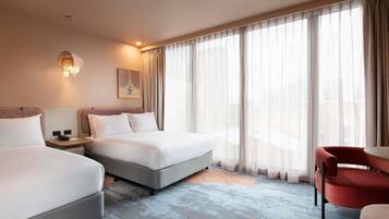 A hotel room with two beds, a desk, a chair, and a large window with curtains.