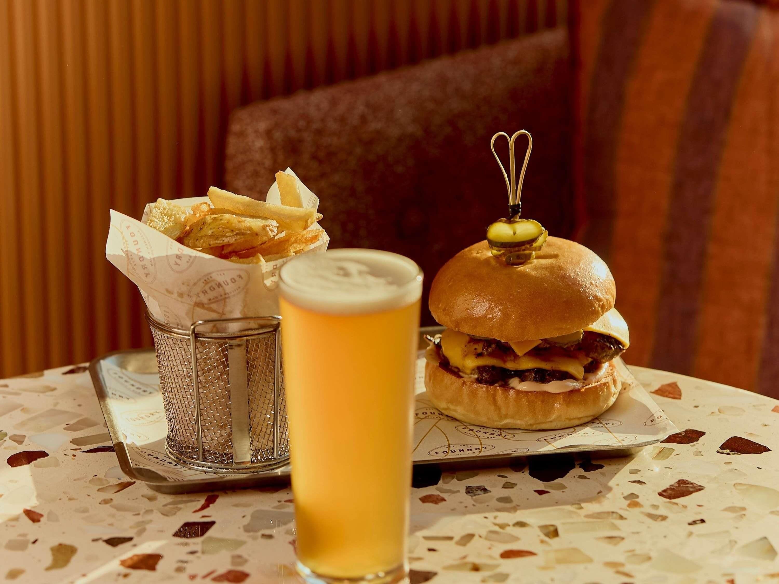 A meal consisting of a burger, fries, and a beer on a table with a patterned tablecloth.