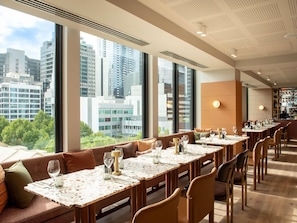 A modern dining area with high ceilings, large windows, and a city view. - Mercure Melbourne La Trobe Street (West Melbourne)