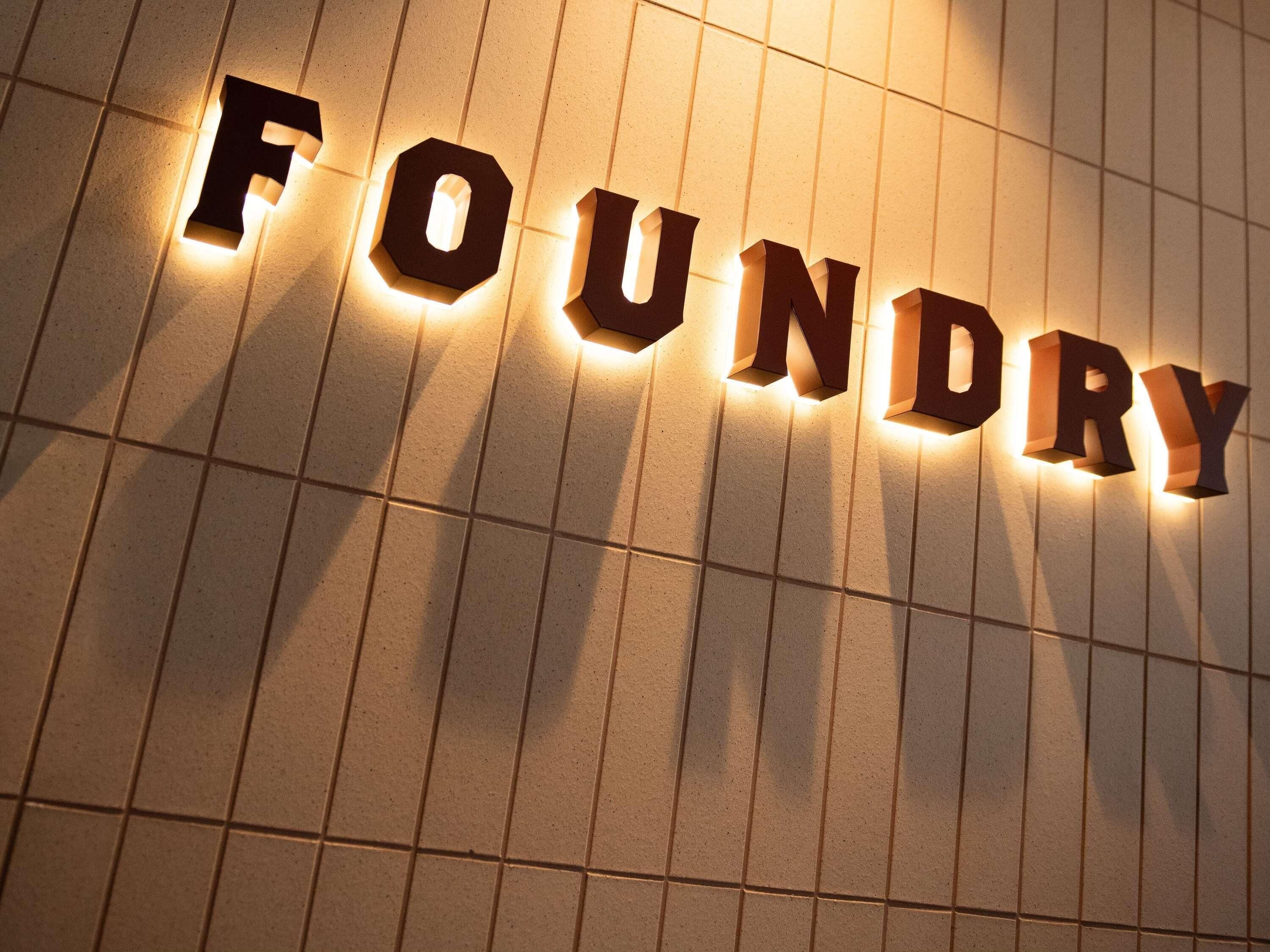 Verlichte letters die 'FOUNDRY' vormen op een betegelde muur.