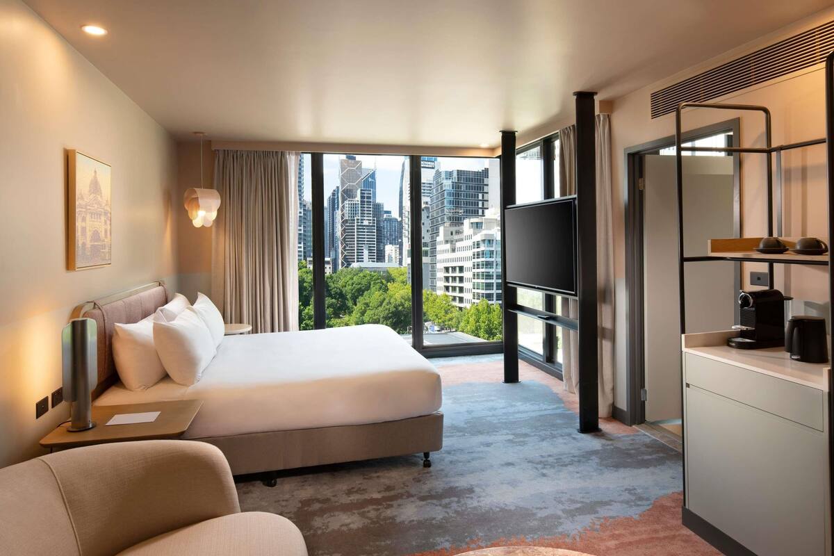 A hotel room with a bed, a desk, a chair, a TV, and a coffee machine.