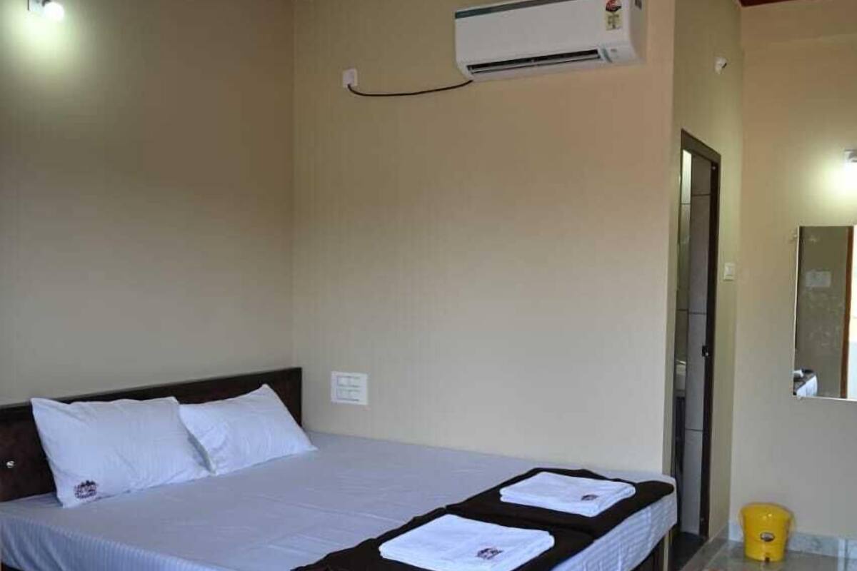 A bedroom with a bed, a ceiling fan, an air conditioning unit, a chair, and a bathroom door.