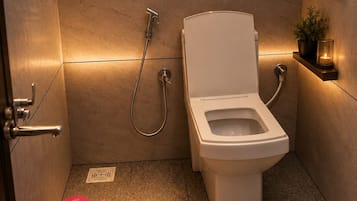 A compact bathroom with a toilet, a shower, and a small shelf with a plant and candle.