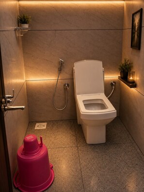 A compact bathroom with a toilet, a shower, and a small shelf with a plant and candle. - Highway Heaven (Bhatkal)