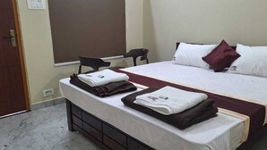 A hotel room with a bed, a chair, a desk, and a small table. - Highway Heaven (Bhatkal)