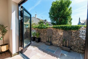 A modern outdoor patio with stone flooring, potted plants, and a stone wall. - Chic Seaside Escape - Steps to Viking Bay & Town (Broadstairs)
