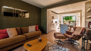 Un salon moderne comprenant un canapé, un fauteuil et un pouf, une table basse en bois et un grand miroir mural.
