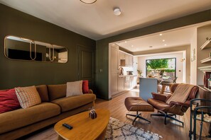 Un salon moderne comprenant un canapé, un fauteuil et un pouf, une table basse en bois et un grand miroir mural.