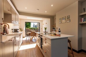 A modern kitchen with a central island, built-in appliances, and a dining area with natural light. - Chic Seaside Escape - Steps to Viking Bay & Town (Broadstairs)