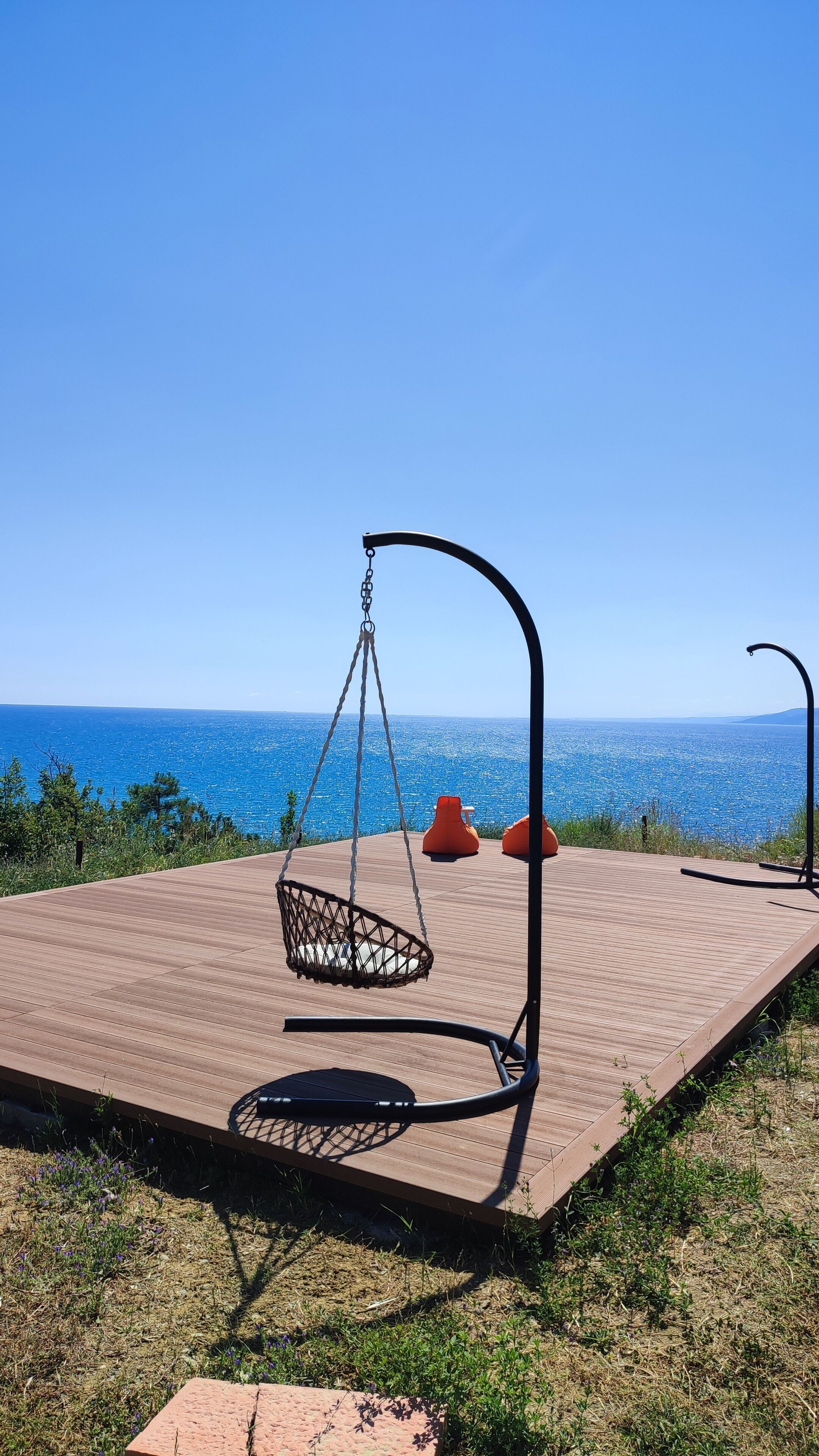 Eine Holzterrasse mit einer hängenden Schaukel, zwei orangenen Sitzsäcken und Blick auf das Meer.