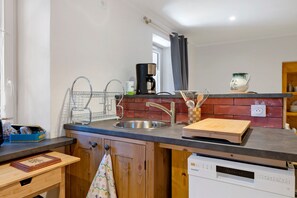 Une cuisine équipée d’un évier en acier inoxydable, d’une machine à café, d’une planche à découper et d’un lave-vaisselle.