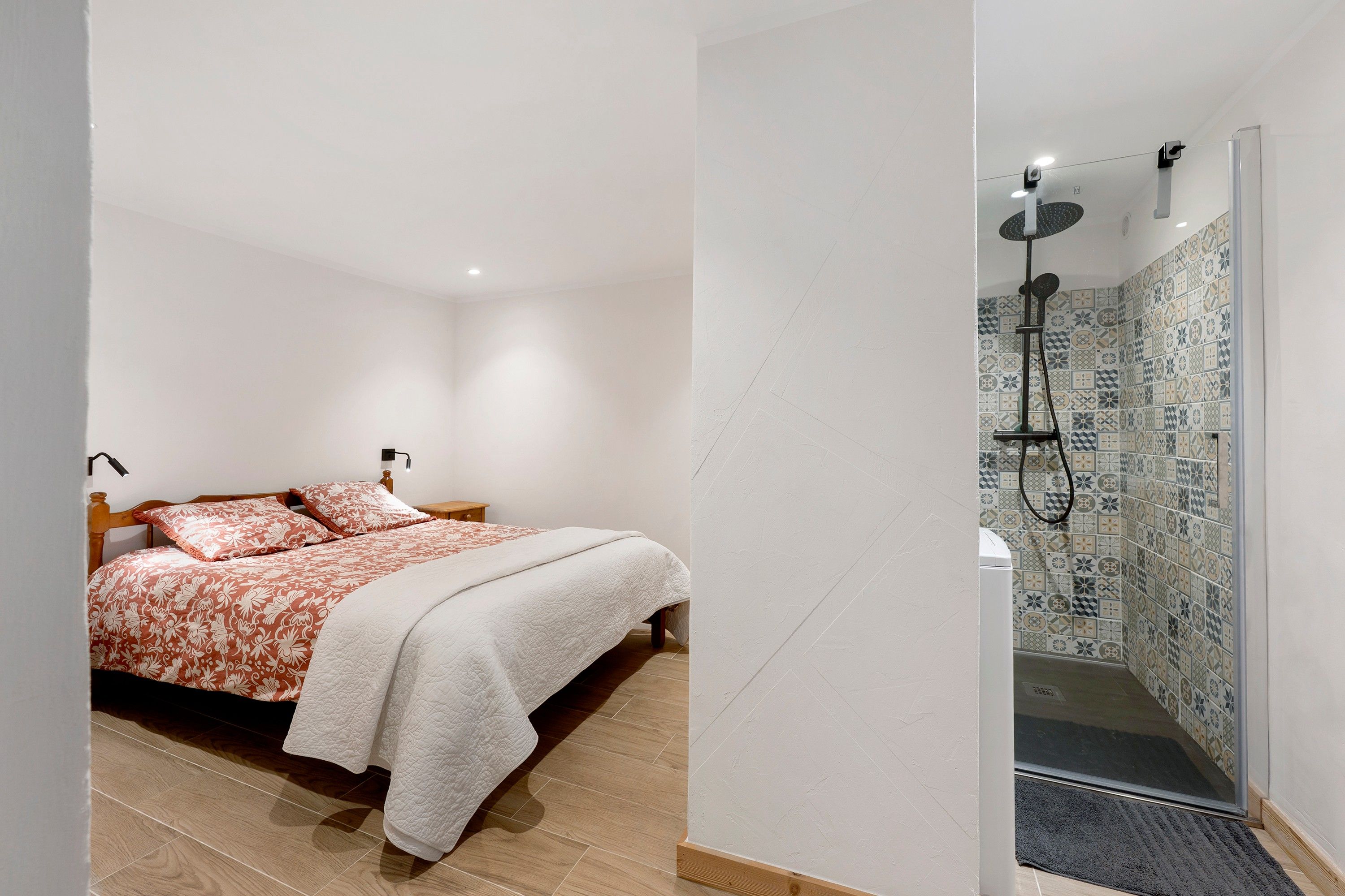 Een slaapkamer met een bed, nachtkastjes en een douchegedeelte met een betegelde muur.