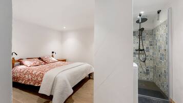 A bedroom with a bed, bedside tables, and a shower area with a tiled wall.