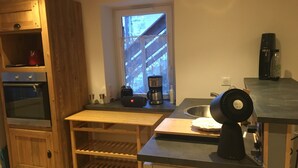 A compact kitchen with a built-in oven, a coffee maker, and a fan on the counter. - Papi Stop with Wi-Fi (Les Belleville)