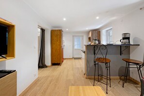 Eine kleine Küche mit einer Holzausstattung, zwei Barhocker, einer Kaffeemaschine und einem Fernseher auf einem Regal.