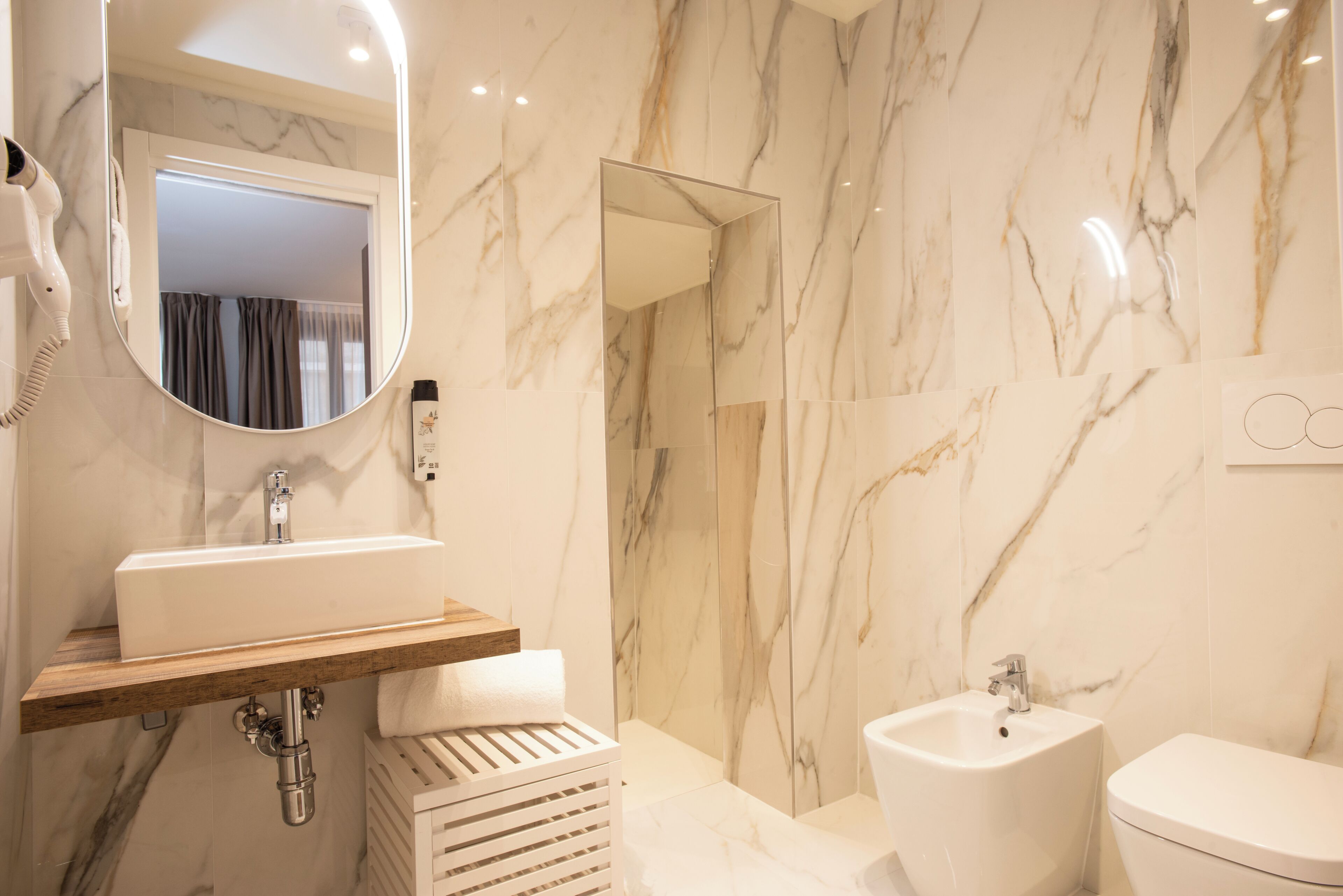 A modern bathroom with a marble wall, a sink, a bidet, and a mirror.