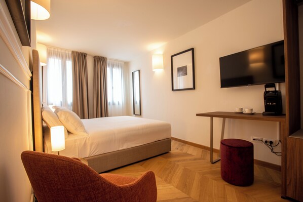 Ein Hotelzimmer mit Bett, Schreibtisch, Fernseher, Stuhl und einem roten Hocker.