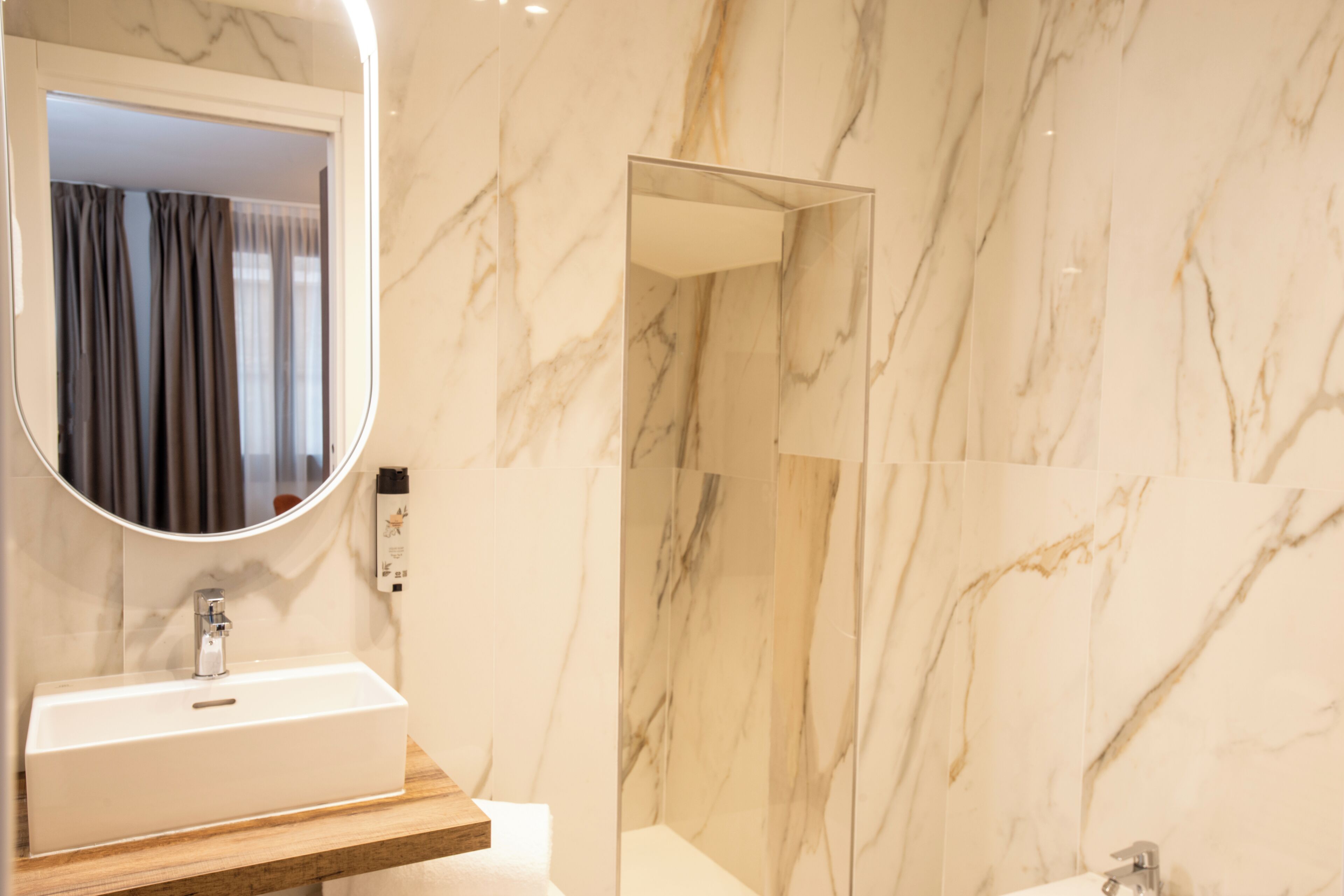 Un baño con pared de mármol, un lavabo con espejo y una zona de ducha.
