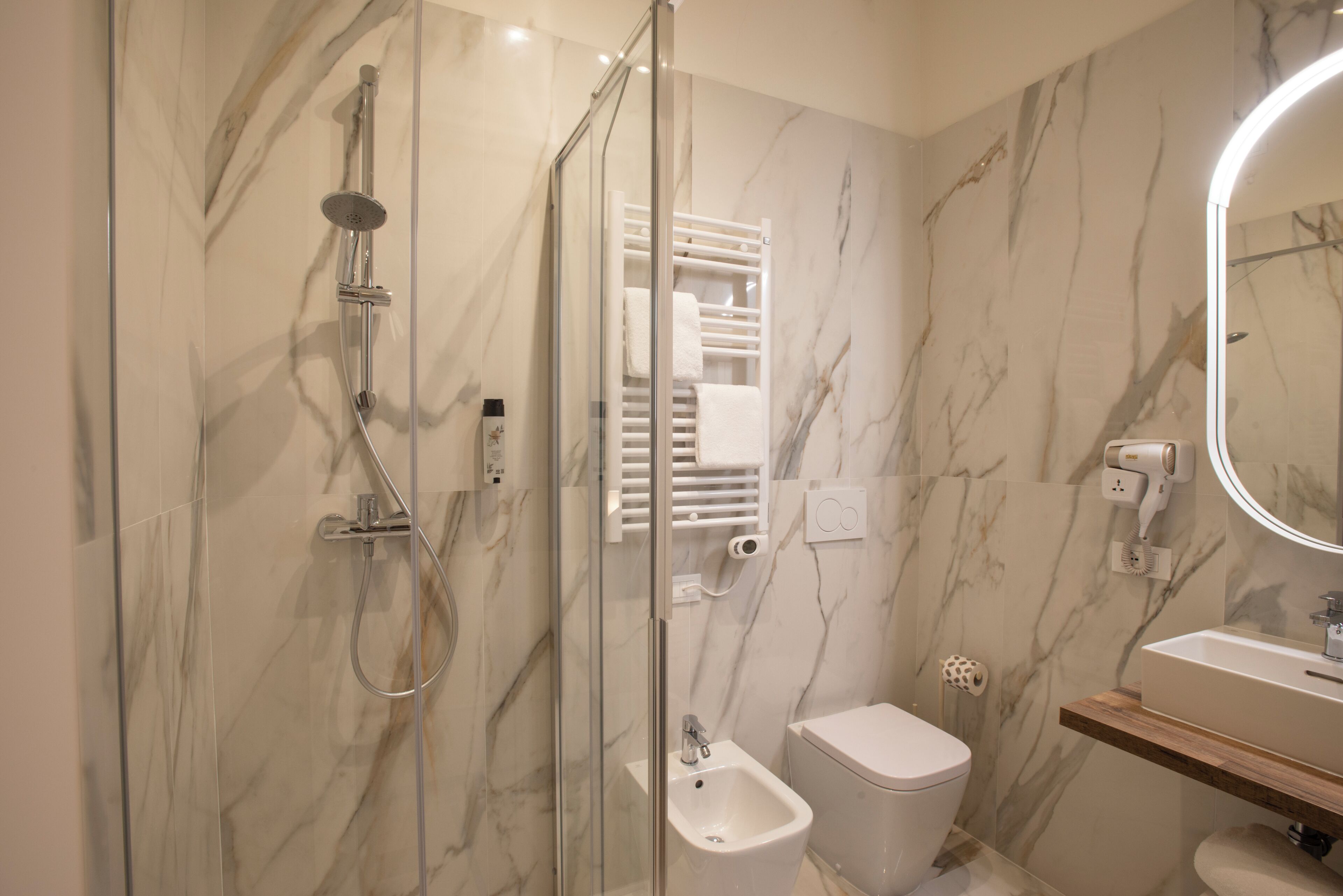 A modern bathroom with a glass-enclosed shower, a bidet, a toilet, a vanity with a mirror, and marble walls.