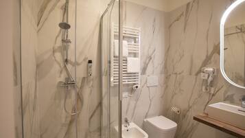 A modern bathroom with a glass-enclosed shower, a bidet, a toilet, a vanity with a mirror, and marble walls.