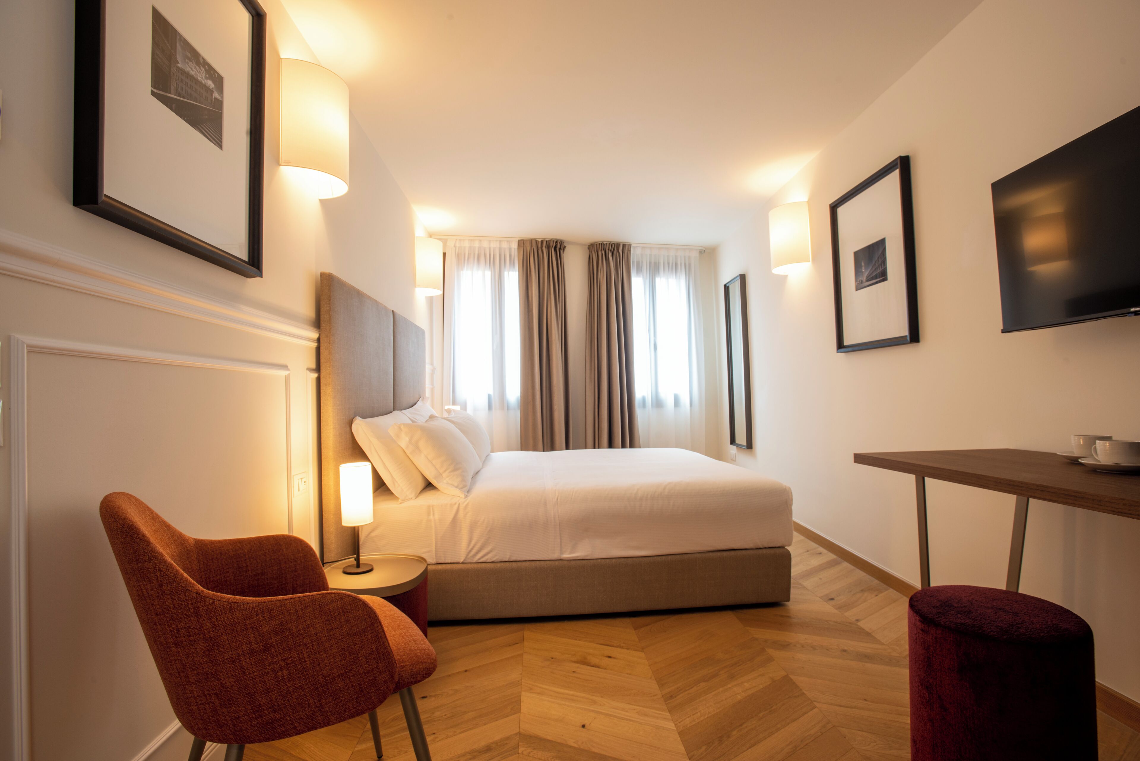 A hotel room with a bed, a desk, a chair, and a TV.